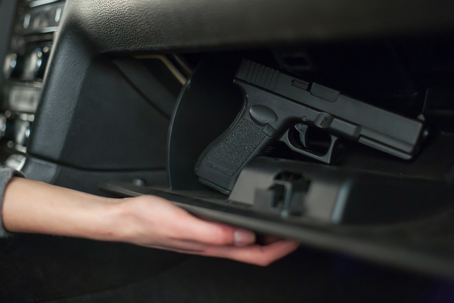 The female hand pulls out a gun from the glove box in the car.