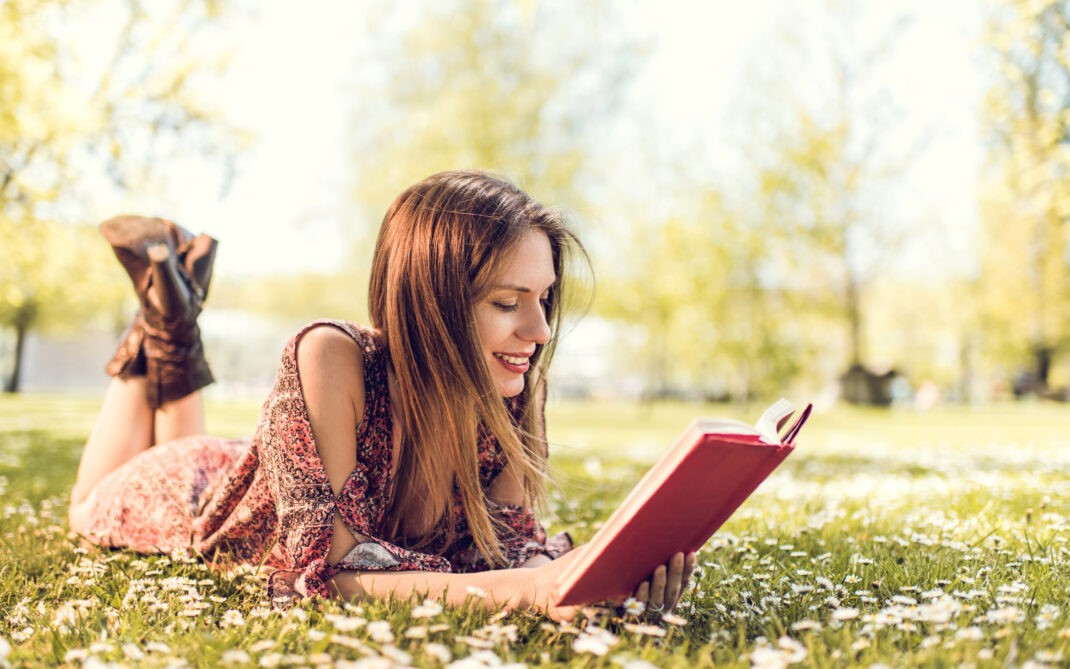 Smiling woman relaxing in grass and reading a book.